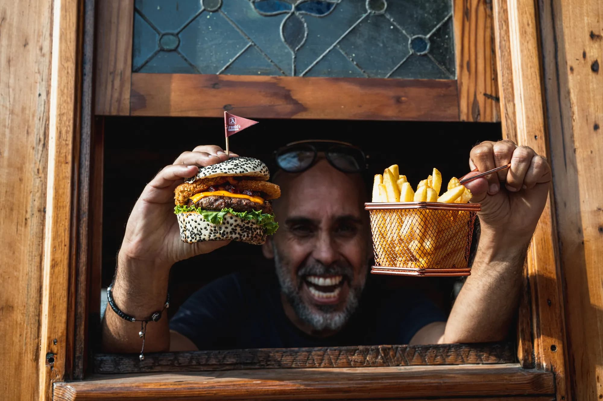 Damián, creador de Arnold's, sonríe en la ventana del tren con una burger y una canasta de papas